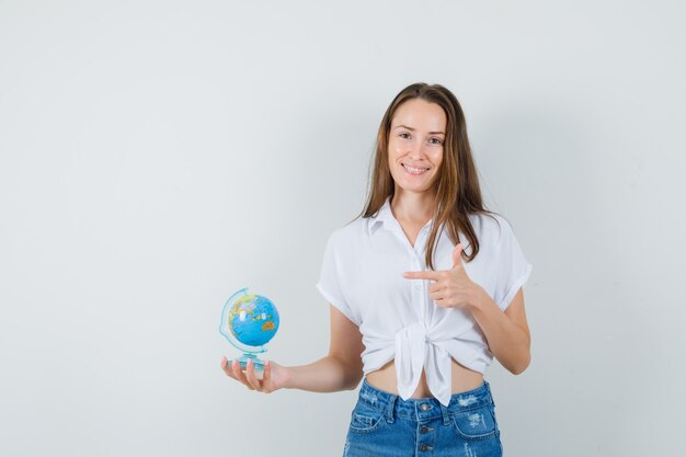 Beautiful lady in white blouse pointing at mini globe , front view.