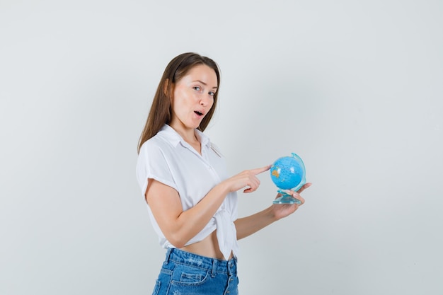 Beautiful lady in white blouse pointing at somewhere on globe and looking talkative , front view.