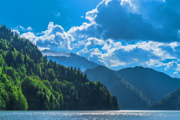 Beautiful Lake Ritsa in the Caucasus Mountains. Green mountain hills, blue sky with clouds. Spring landscape.