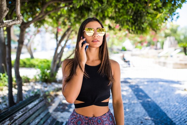 Красивая латинская женщина разговаривает по телефону и улыбается в парке