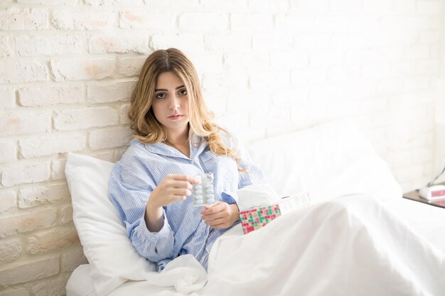 無料写真 ベッドに座って気分が悪くなり、薬を飲んでいる美しいラテン系の若い女性