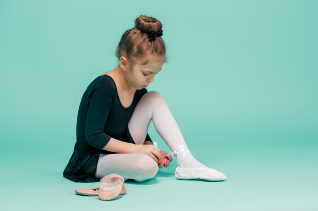 Beautiful little ballerina in black dress for dancing puting on foot pointe shoes