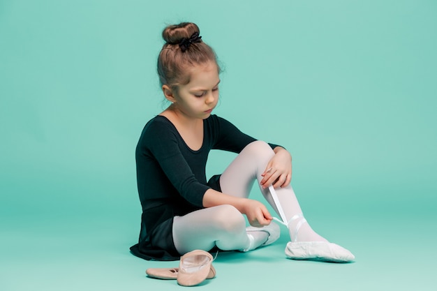 Beautiful little ballerina in black dress for dancing puting on foot pointe shoes