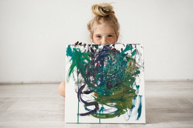 beautiful little blonde girl holding and hiding by the big picture