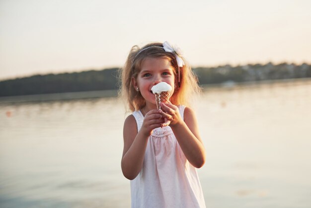 Красивая маленькая девочка ест мороженое у воды