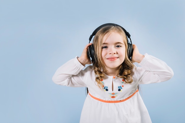 Beautiful little girl enjoying the music on headphone against blue backdrop