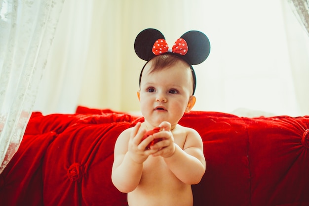 미니 마우스 귀에 아름다운 소녀는 밝은 방에서 빨간 침대 앞에 서 프리미엄 사진