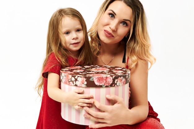 Beautiful little girl posing isolated with her young mother holding fancy box, giving it to you for birthday