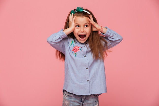 Бесплатное фото Красивая маленькая девочка реагирует эмоционально хватая голову обеими руками в восторге и шоке