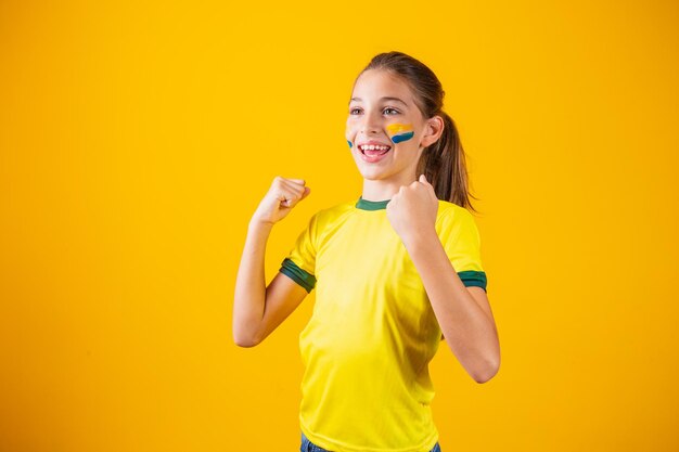 黄色の背景で彼女のチームを応援している美しい少女。ゴールを祝い、ブラジルの勝利を祝う少女