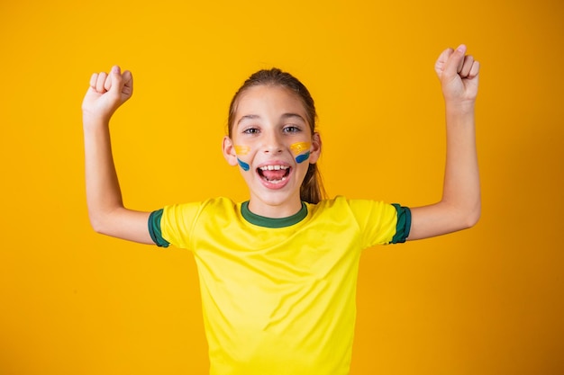 Beautiful little girl rooting for her team on yellow background. little girl celebrating the goal and celebrating brazil's victory