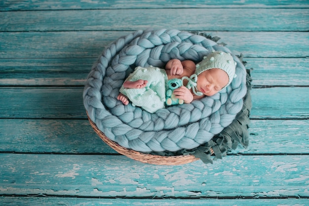 Beautiful little girl sleeps with blue bear on blue blanket in the basket 