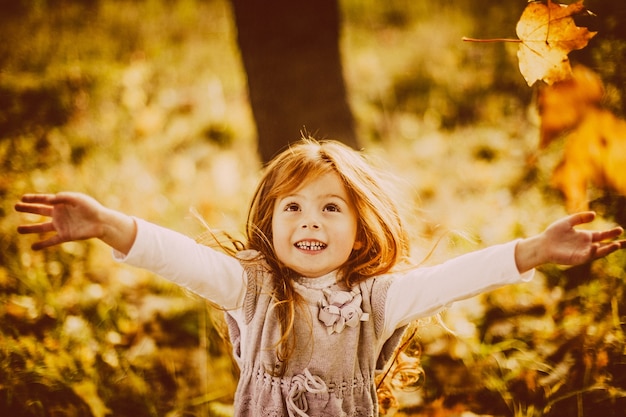 Beautiful little girl with red hair looks happy playing with fallen leaves 