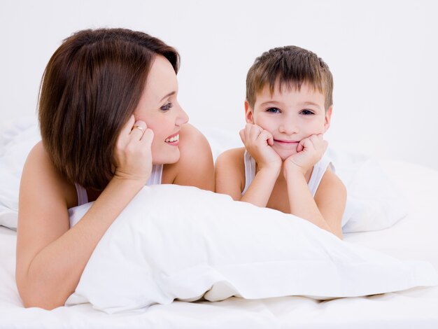 행복 웃는 어머니가 침대에 누워 카메라를보고 아름다운 작은 아이