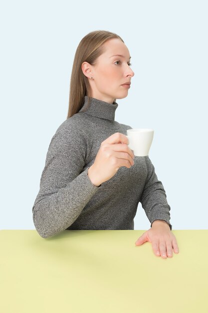 一杯のコーヒーを手に持って座って悲しそうに見える美しい孤独な女性。ミニマリズムスタイルのクローズアップトーンの肖像画