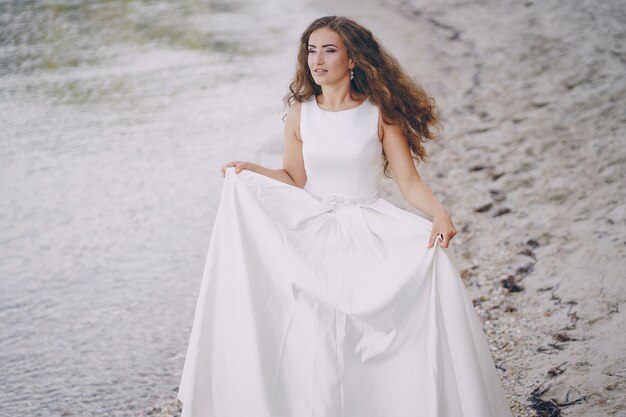 ビーチで歩く壮大な白いドレスの美しい長髪の花嫁