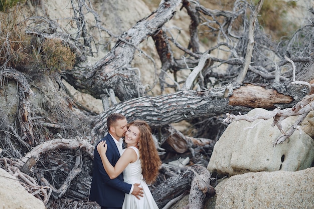 beautiful long-haired bride in white dress with her husband near gray branches