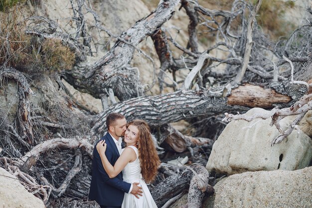 beautiful long-haired bride in white dress with her husband near gray branches