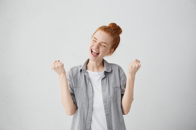 Free photo beautiful lucky european girl feeling excited and happy, closing eyes tight in pleasure, keeping mouth opened and fists clenched