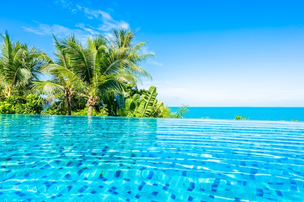 ココヤシの木と青い空に白い雲の周りの海とホテルリゾートの美しい高級屋外スイミングプール