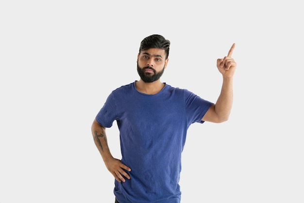 Beautiful male half-length portrait isolated on white studio background. Young emotional hindu man in blue shirt. Facial expression, human emotions, advertising concept. Pointing and choosing.