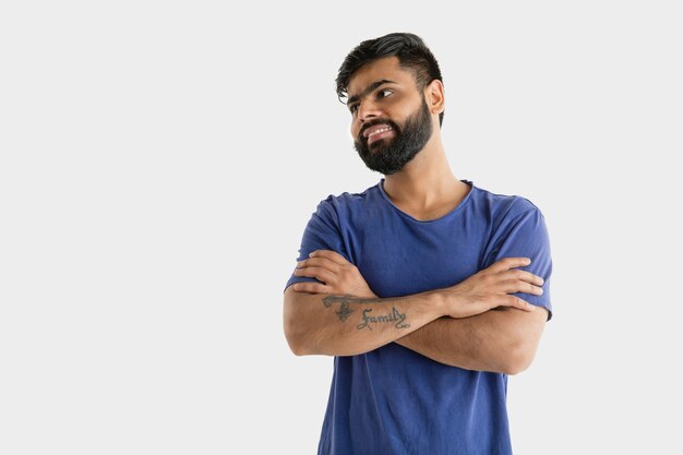 Beautiful male half-length portrait isolated on white studio background. Young emotional hindu man. Facial expression, human emotions, ad concept. Smiling, standing confident with crossed hands.