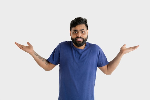 Beautiful male half-length portrait isolated on white wall. Young emotional hindu man in blue shirt. Facial expression, human emotions, advertising concept. Presenting and inviting.