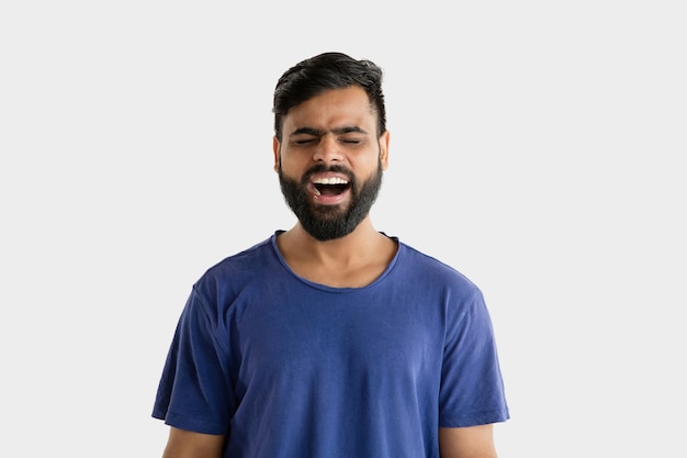Beautiful male half-length portrait isolated on white wall. Young emotional hindu man in blue shirt. Facial expression, human emotions, advertising concept. Screaming or laughting.