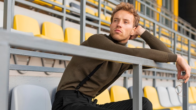 Foto gratuita bellissimo modello maschile seduto in uno stadio