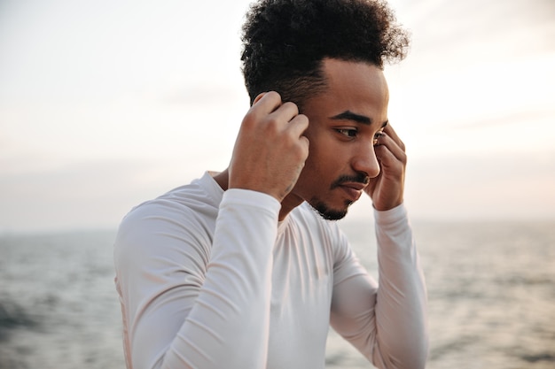 Beautiful man in white long-sleeved t-skirt puts on wireless headphones