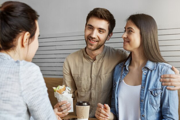Beautiful man with dark hair in stylish clothes introducing his girlfriend to mother in cafe. They drinking coffee, eating, laughing and talking about future.