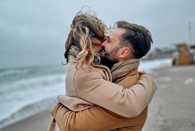 寒い​季節​に​コート​を​着て​、​海岸​に​寄り添う​美しい​夫婦​。