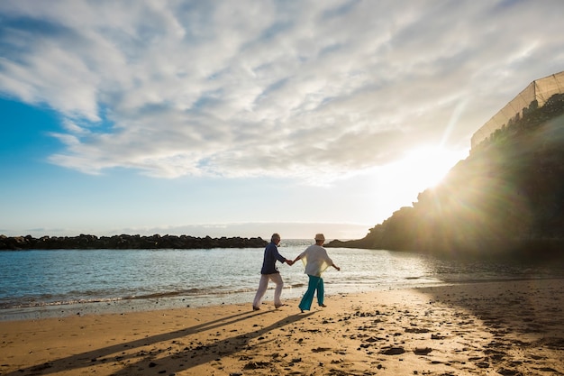 レジャー活動で屋外の美しい成熟したカップルは、海岸のビーチで手をつないで一緒に永遠に一緒に暮らす