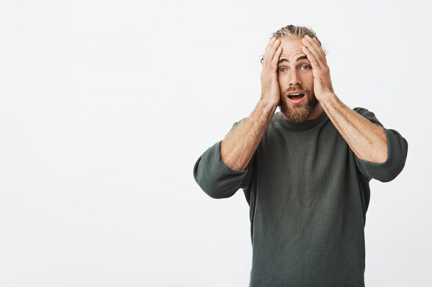 Beautiful mature husband with beard holding hands on head with happy excitement