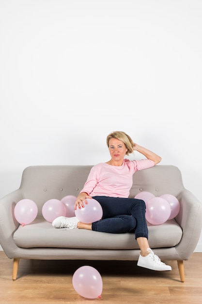 Bella donna matura che si siede sul divano con palloncini rosa