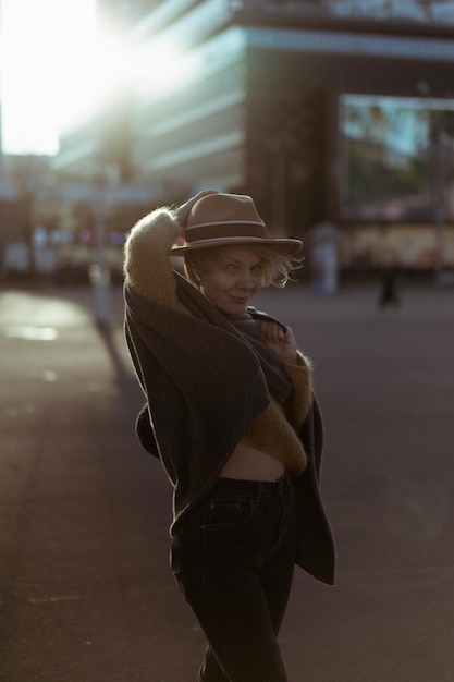 Bella donna di mezza età con un cappello con un taglio di capelli corto nel centro di una grande città. ritratto ravvicinato, controluce soffusa.