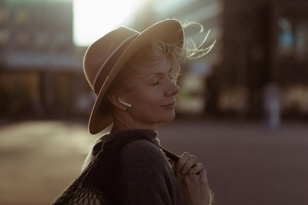Beautiful middle-aged woman in a hat with a short haircut in the center of a big city. Close-up portrait, soft backlight.
