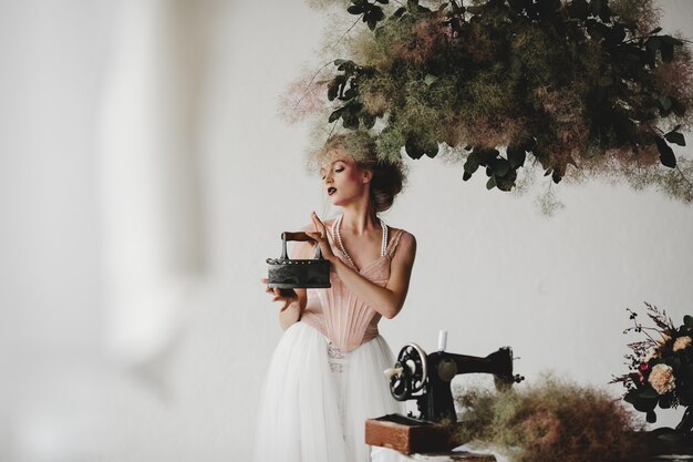 Beautiful model stands with an old iron among beautiful bouquets in the room