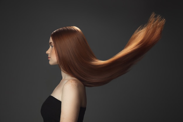 Beautiful model with long smooth, flying red hair isolated on dark