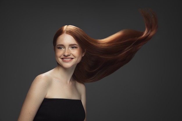 Beautiful model with long smooth, flying red hair isolated on dark