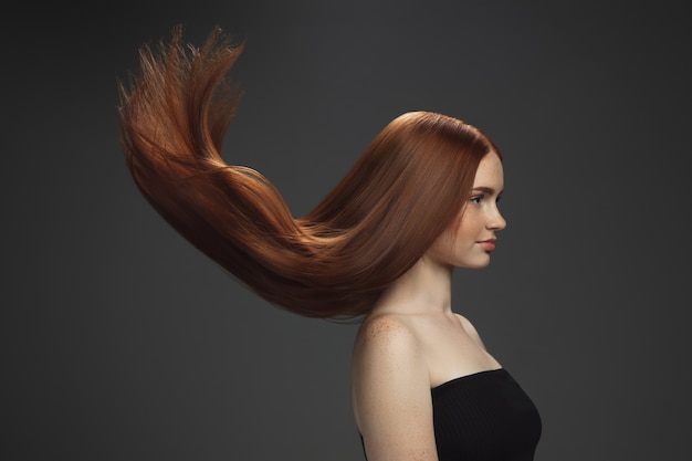 Красивая модель с длинными гладкими, развевающимися рыжими волосами, изолированными на темноте