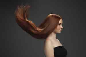 Бесплатное фото Красивая модель с длинными гладкими, развевающимися рыжими волосами, изолированными на темноте