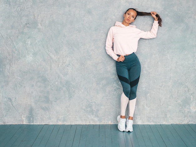 Foto gratuita bellissima modella con un corpo abbronzato perfetto. donna in posa in studio vicino al muro grigio. tenendo i capelli in mano