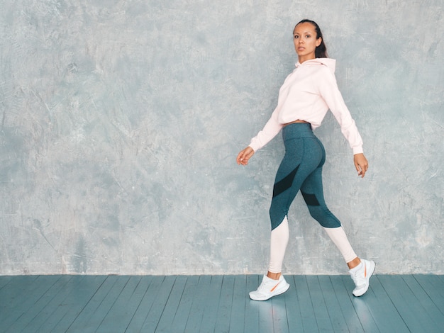 Beautiful model with perfect tanned body.Female walking in studio near gray wall