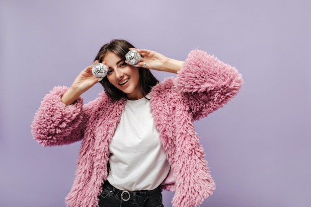 Foto gratuita bella ragazza moderna con capelli lunghi scuri in jeans neri con maglietta leggera da cintura e maglione caldo ed elegante che sorride e tiene le palle da discoteca