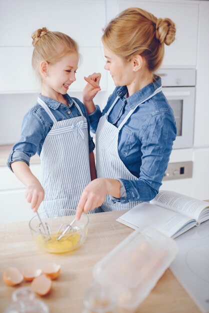 ブルーシャツとエプロンの美しい母親は台所で家で夕食を準備しています