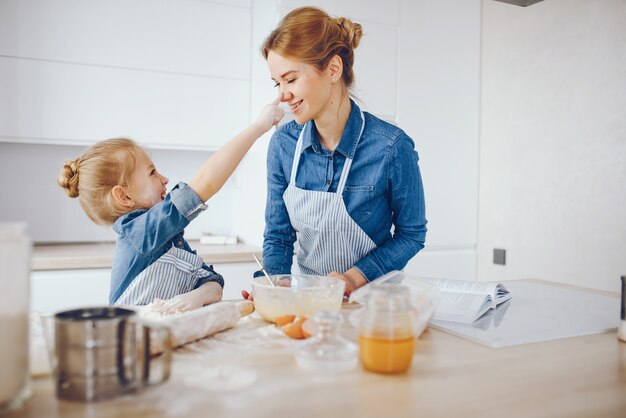 파란색 셔츠와 앞치마에 아름다운 어머니는 부엌에서 집에서 저녁 식사를 준비하고있다
