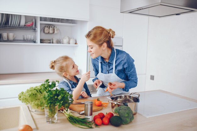 красивая мать в синей рубашке и фартуке готовит свежий овощной салат дома