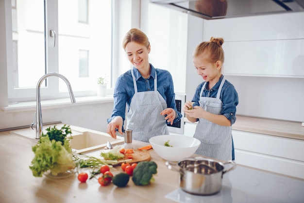 beautiful mother in a blue shirt and apron is preparing a fresh vegetable salad at home 