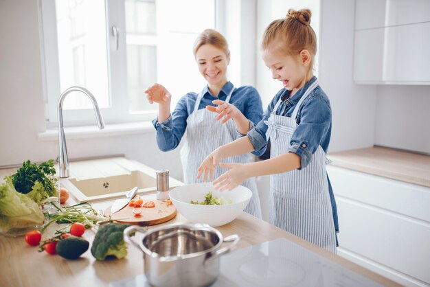 파란색 셔츠와 앞치마에 아름다운 어머니는 집에서 신선한 야채 샐러드를 준비하고있다
